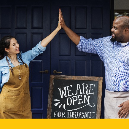 Two migrant business owners high five in front of their shop 