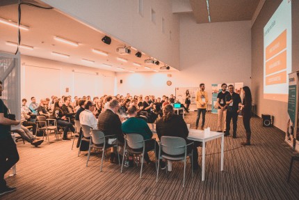 Large audience listens to 4 people giving a presentation Large audience listens to 4 people giving a presentation