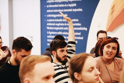 A young man raises his hand in the crowd to ask a  question 